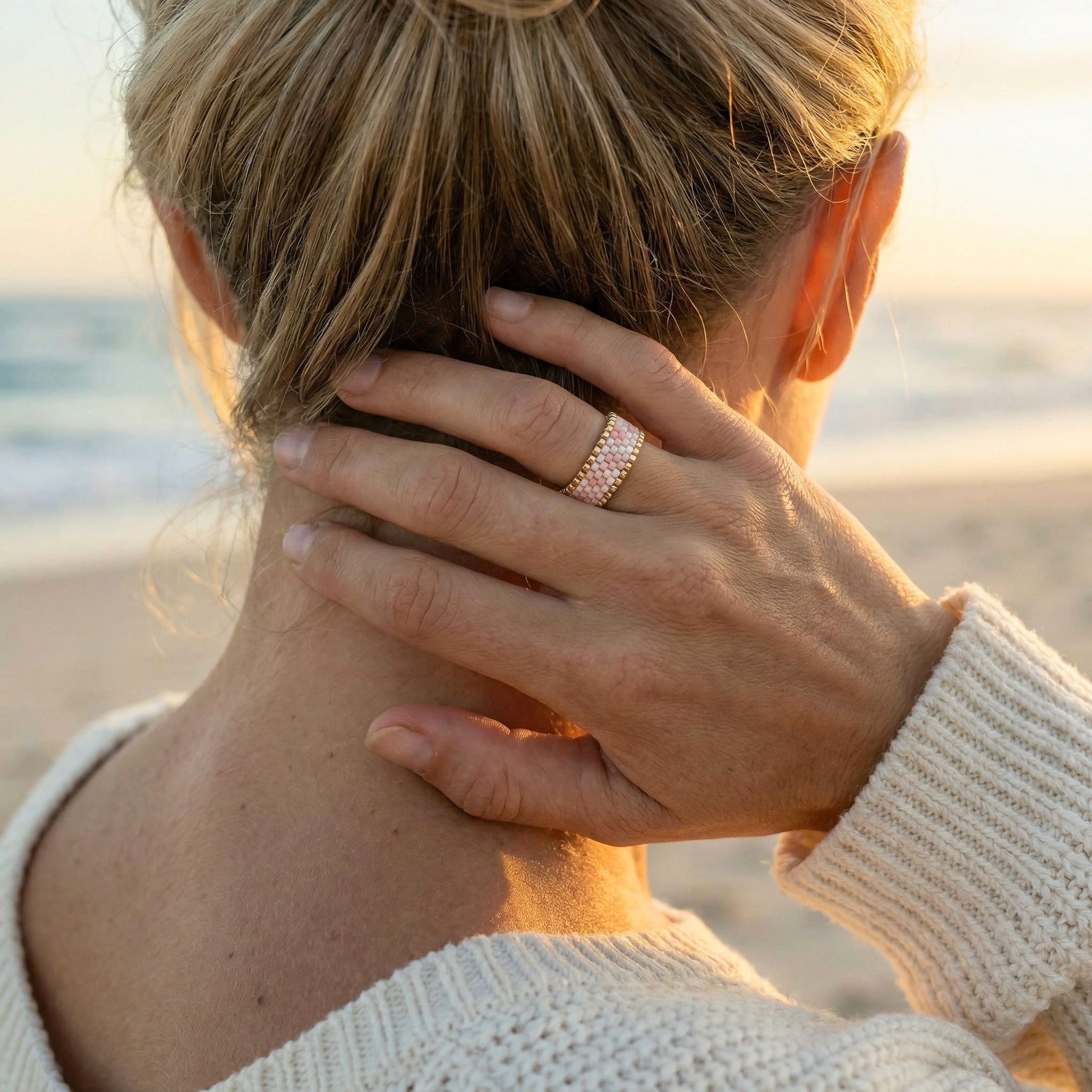 Person on a beach with hand on neck, wearing a ring