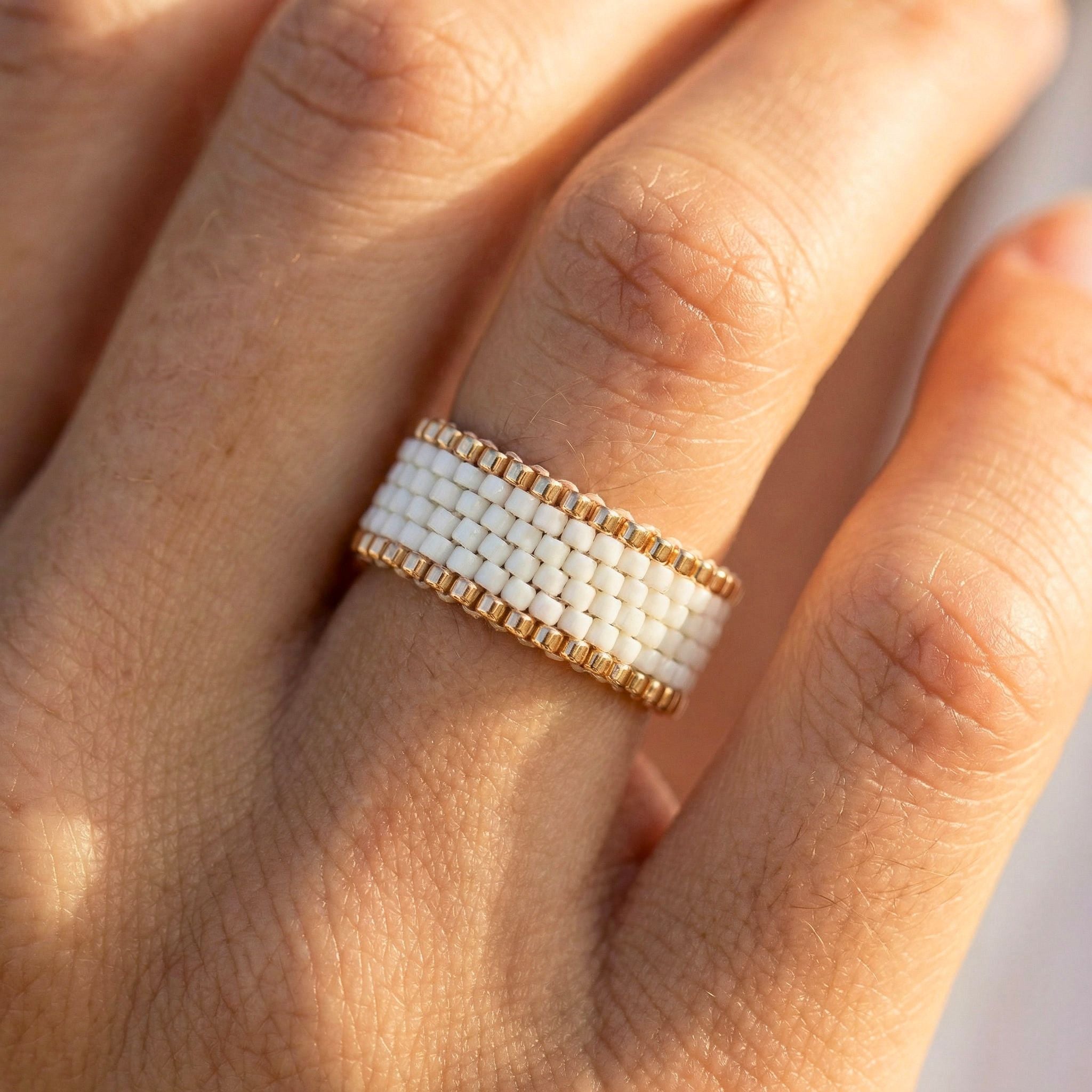 Close-up of a hand wearing a white beaded ring with gold accents.