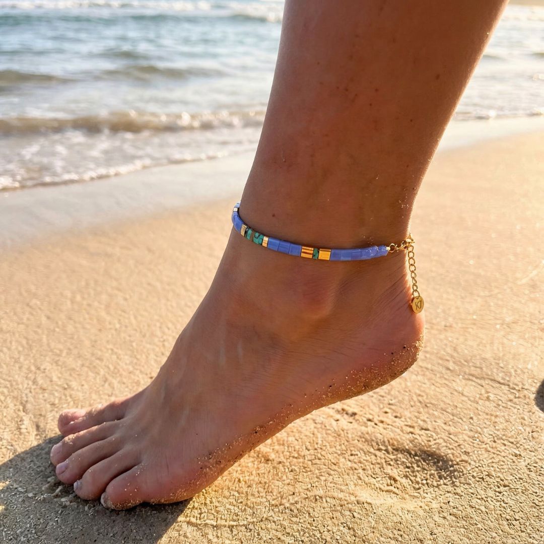 Anchored foot on sand with a colorful anklet, ocean in the background