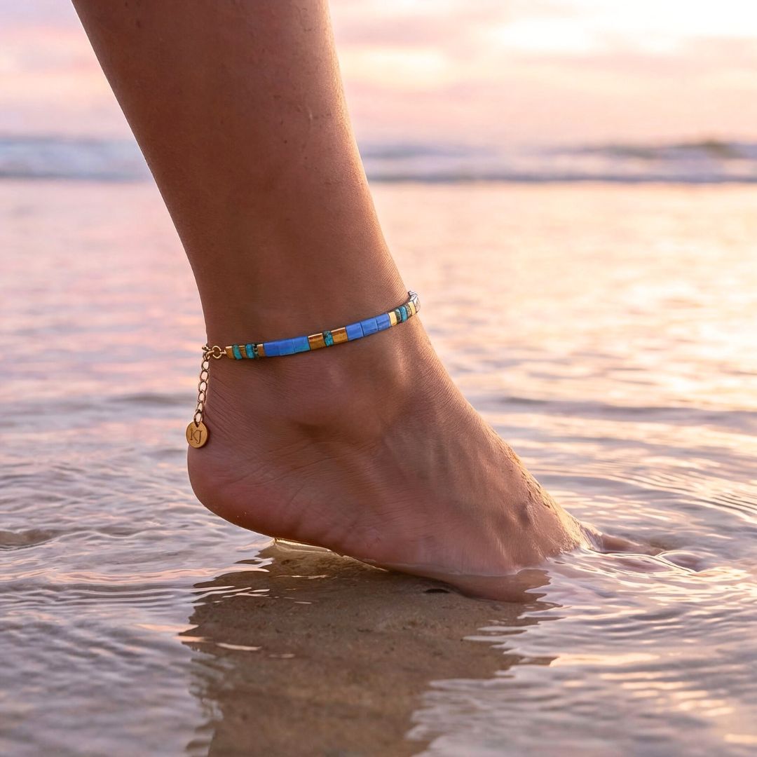 Anchored foot with a blue anklet in shallow water at sunset.