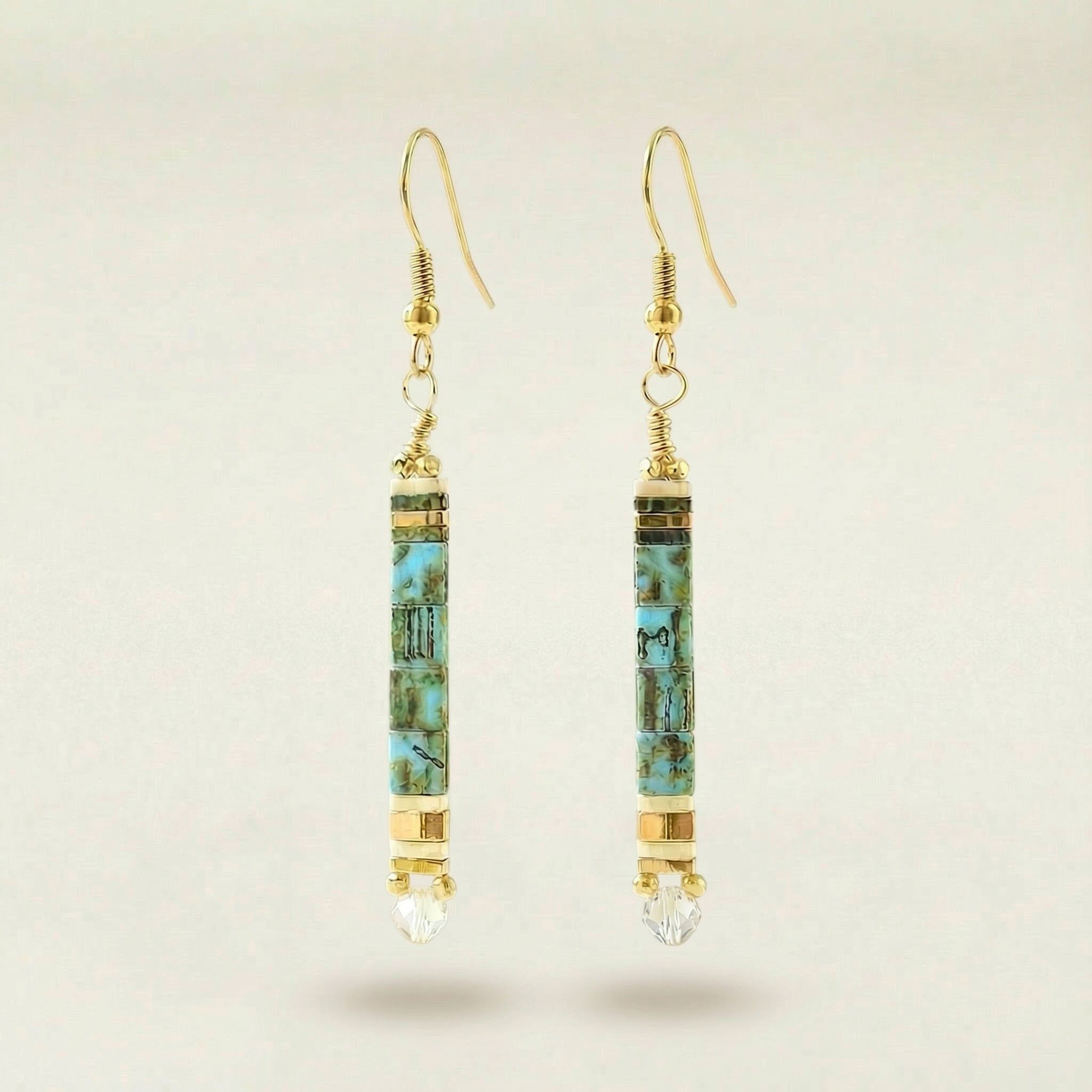 Gold and turquoise earrings on a beige background