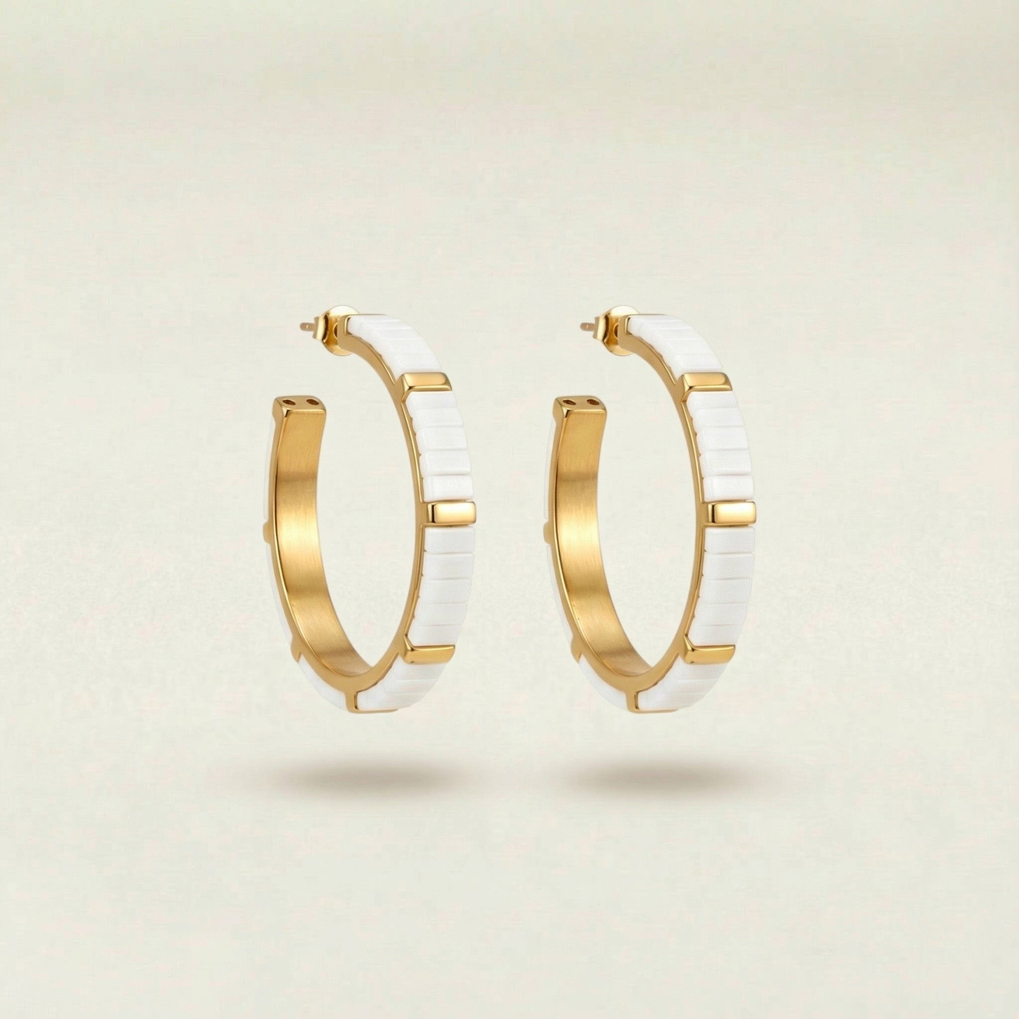 Gold hoop earrings with white ceramic accents on a beige background