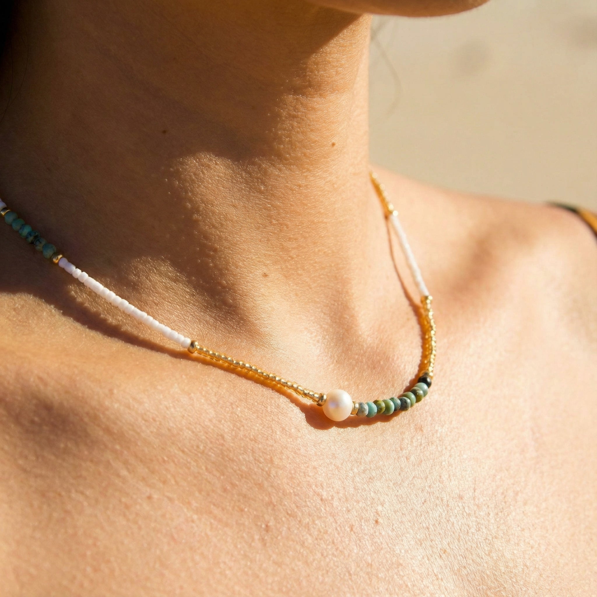 Necklace with beads and a pearl on a person's neck against a blurred background