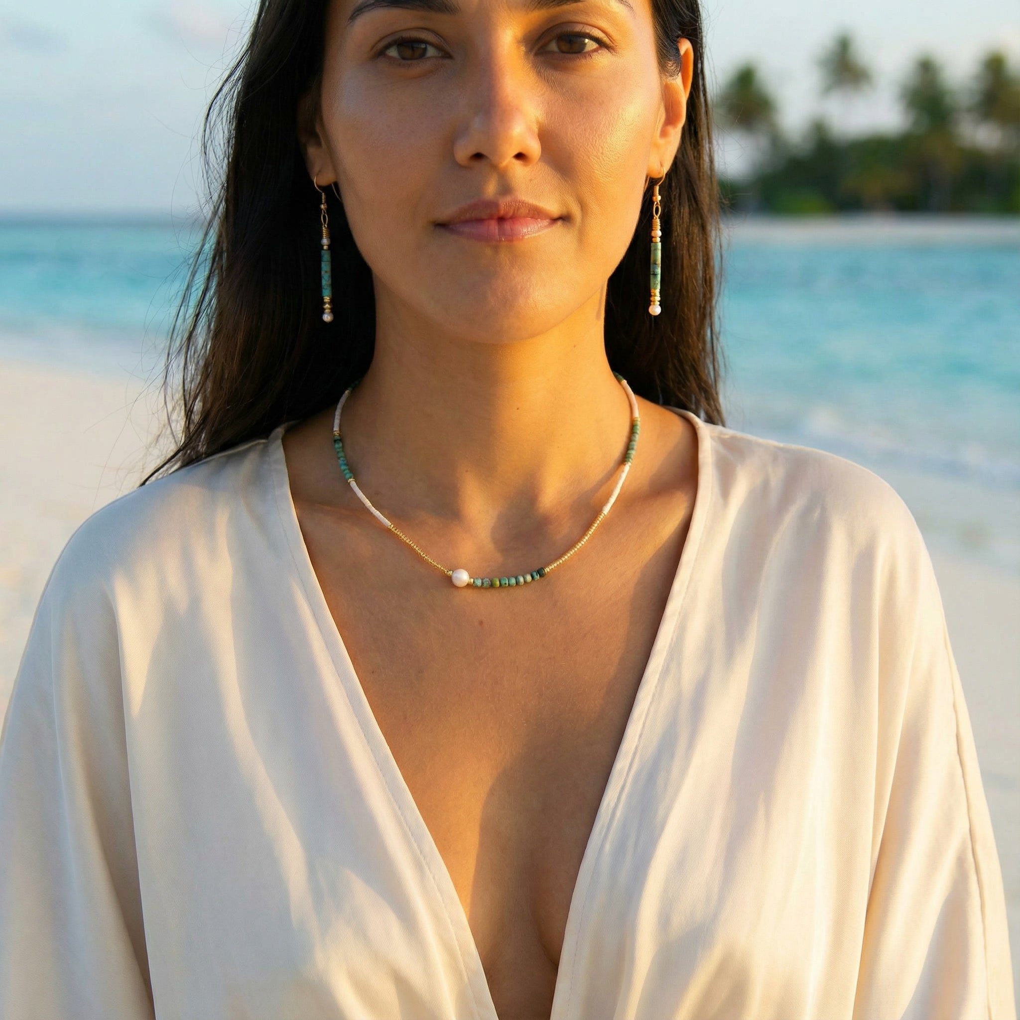 Woman wearing a white top and green necklace with a beach and palm trees in the background