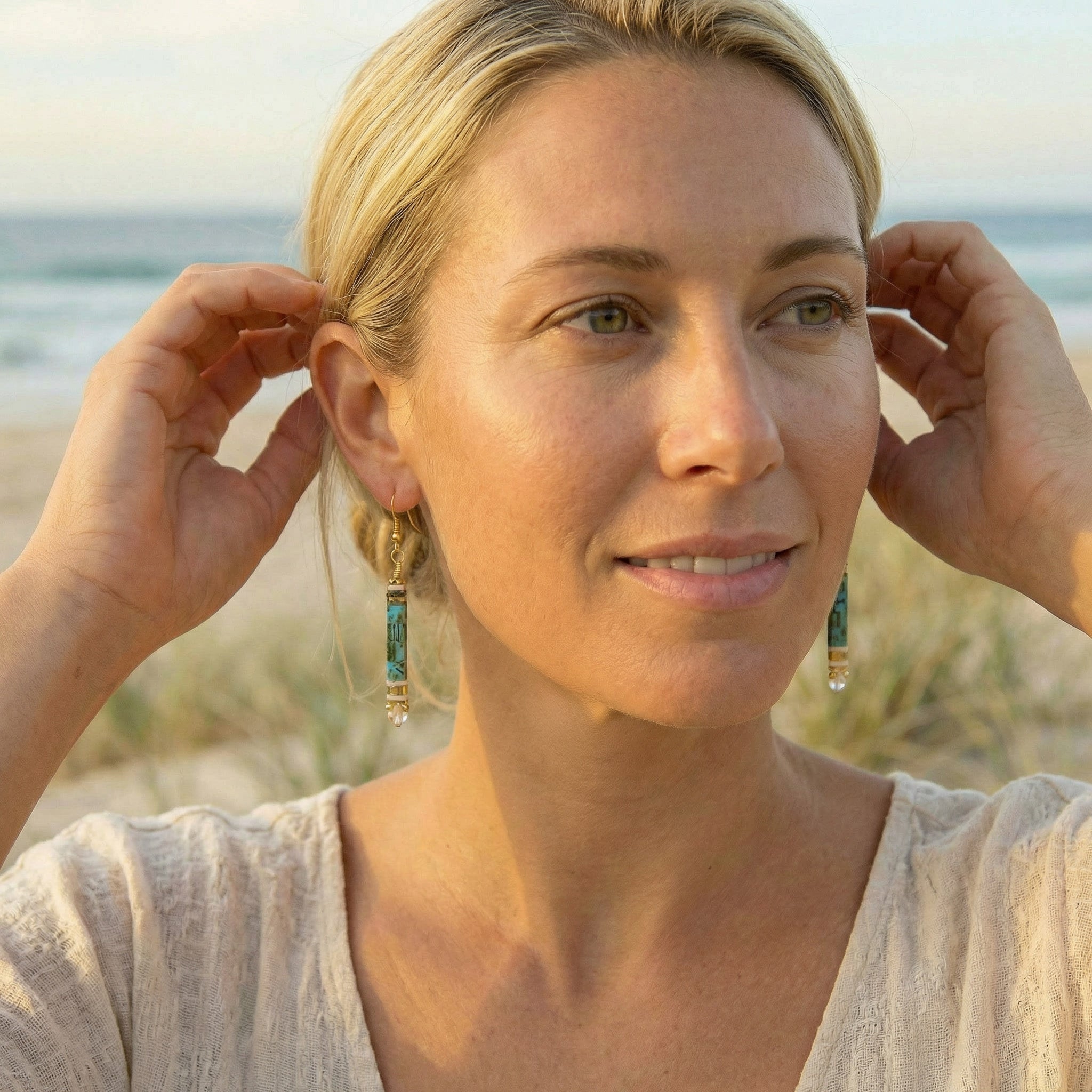 Woman adjusting earrings with a beach background
