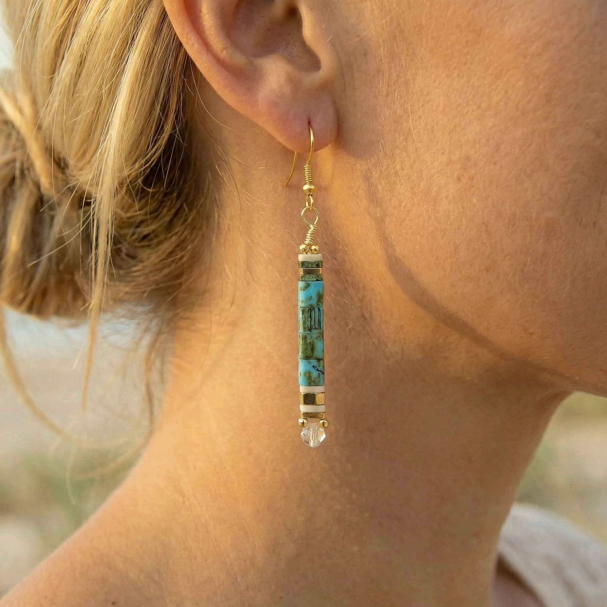 Close-up of a person wearing a turquoise and gold earring outdoors.