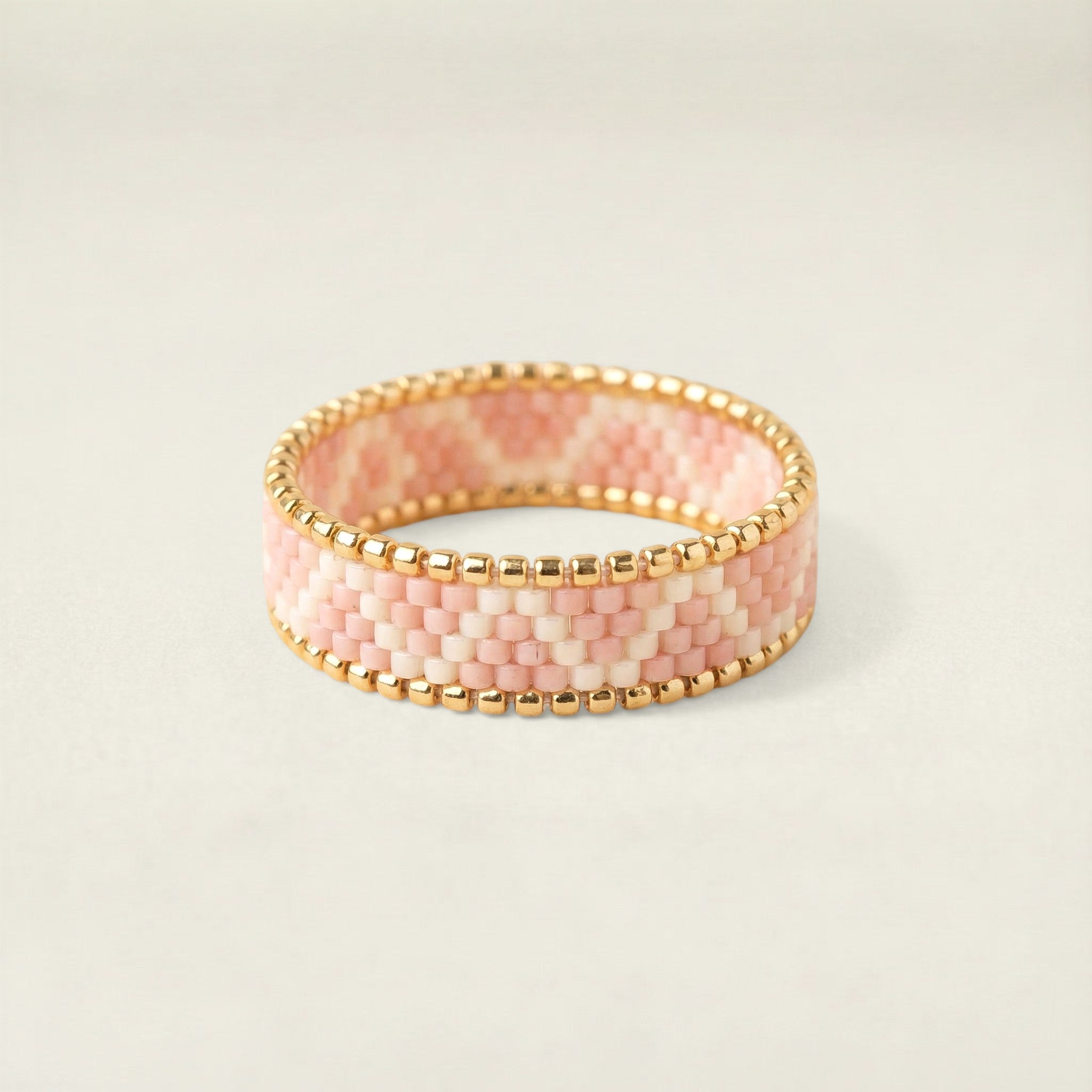 Pink beaded bracelet with gold accents on a light beige background