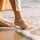 Person's foot with anklet standing in shallow water on a beach