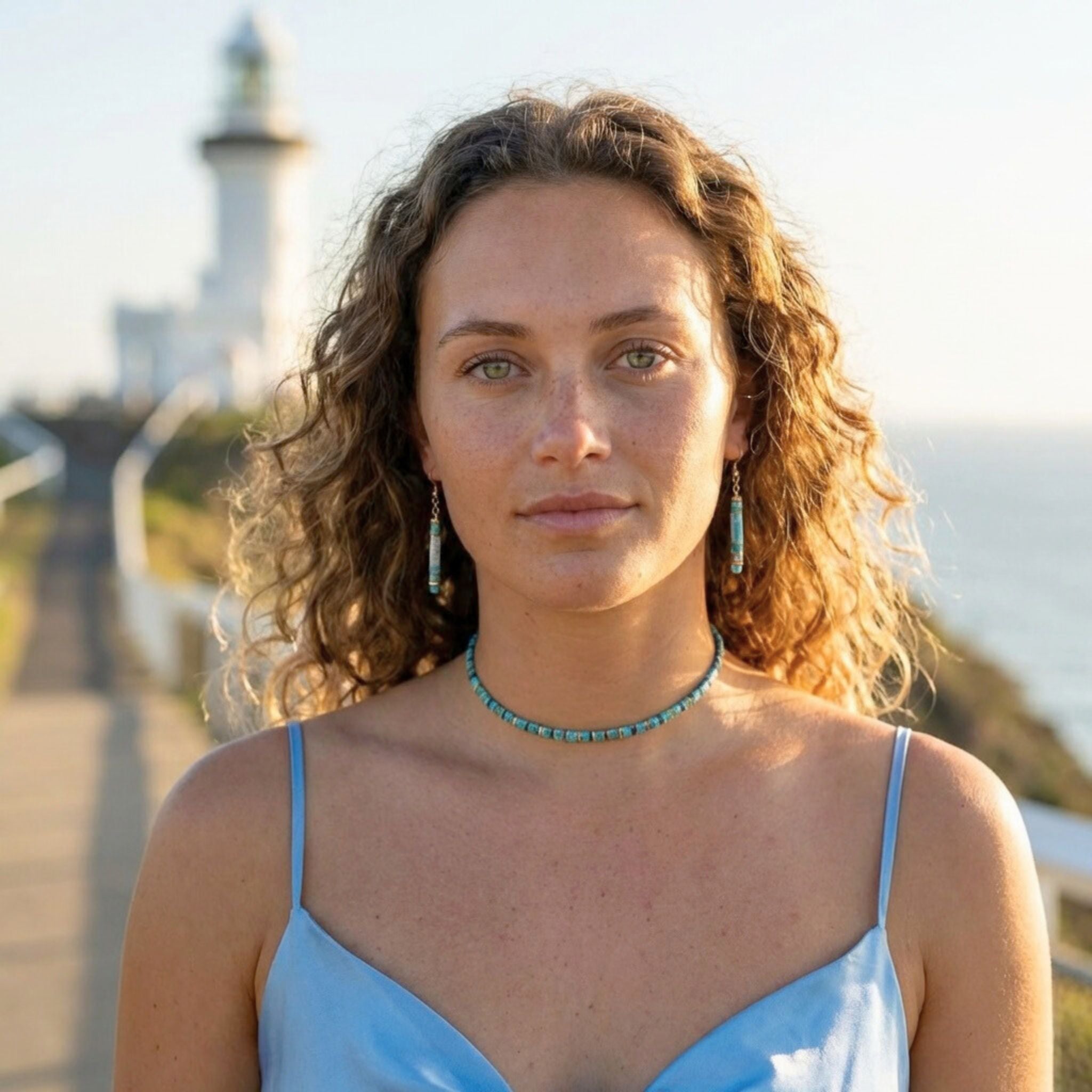 Woman with curly hair and a blue top standing in front of a lighthouse.