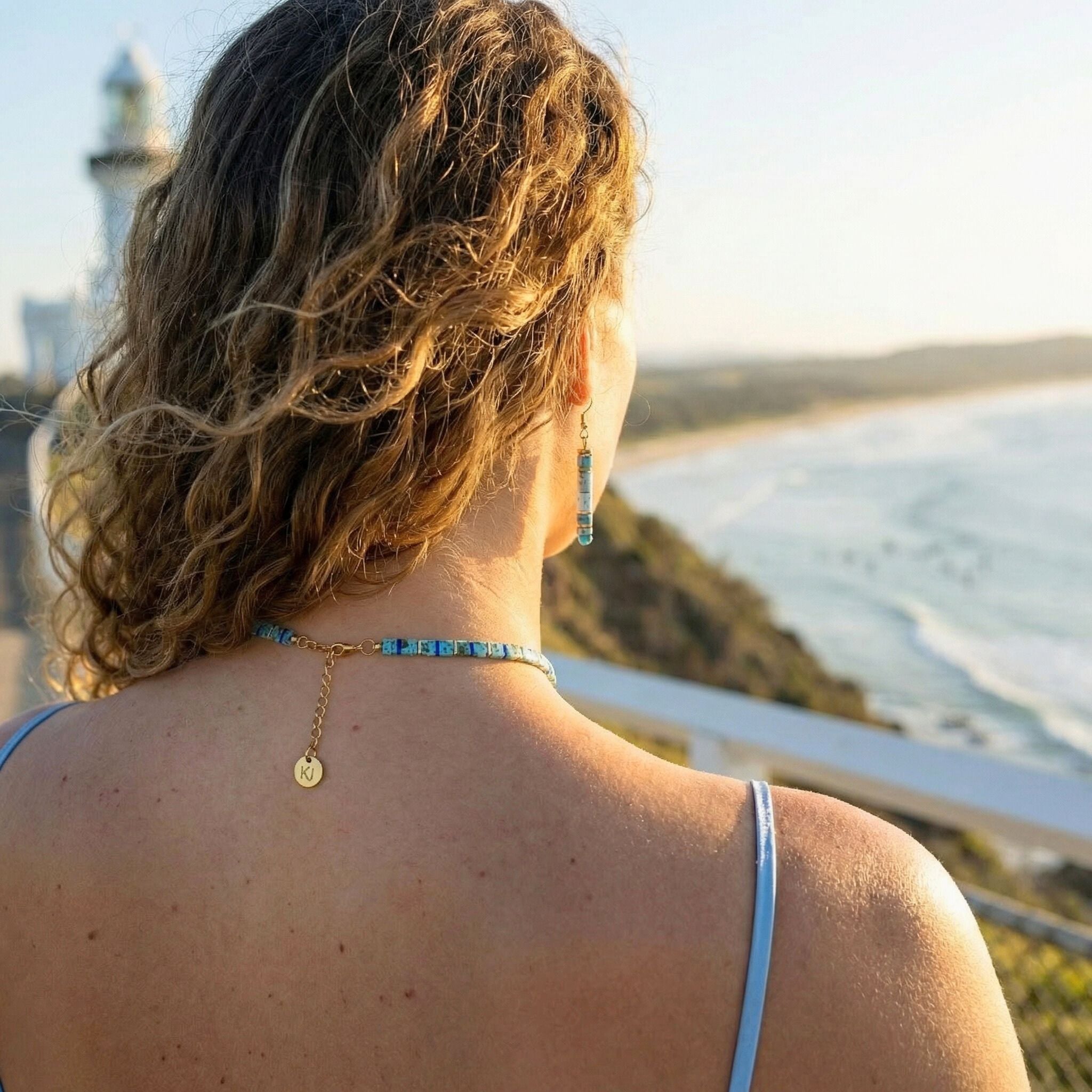 Woman with a necklace overlooking a scenic coastal view with a lighthouse.