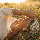 Woman lying in a field with sunset light, wearing a white blouse and floral headband.