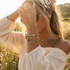 Woman in a field wearing sunglasses, a headband, and a white off-shoulder top with visible jewelry.