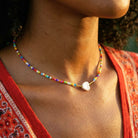 Colorful beaded necklace with a pearl pendant worn by a person in a red garment.