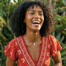 Woman in a red floral dress laughing outdoors with greenery in the background