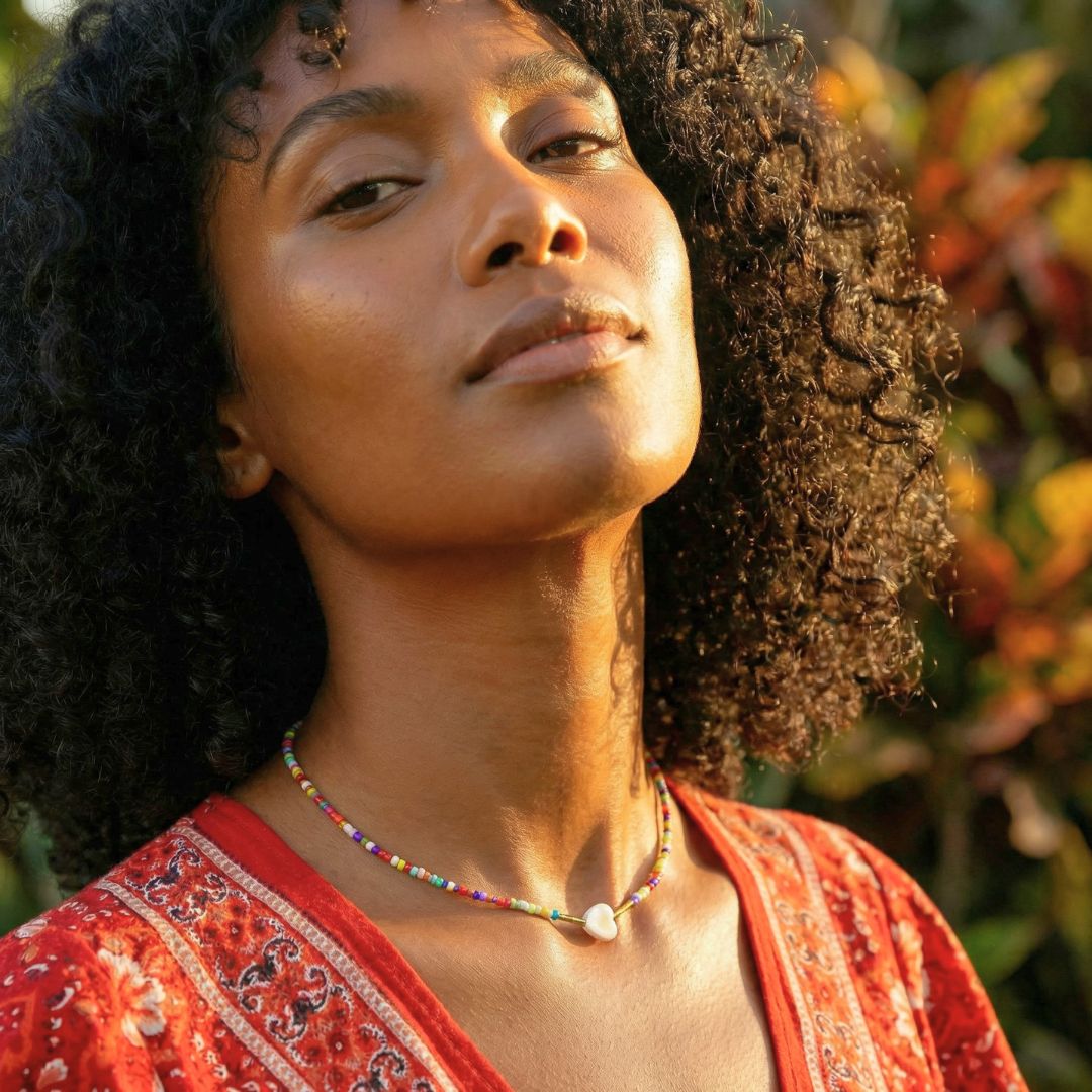 Woman with curly hair wearing a red top and colorful necklace against a natural background