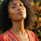 Woman with curly hair wearing a red top and colorful necklace against a natural background