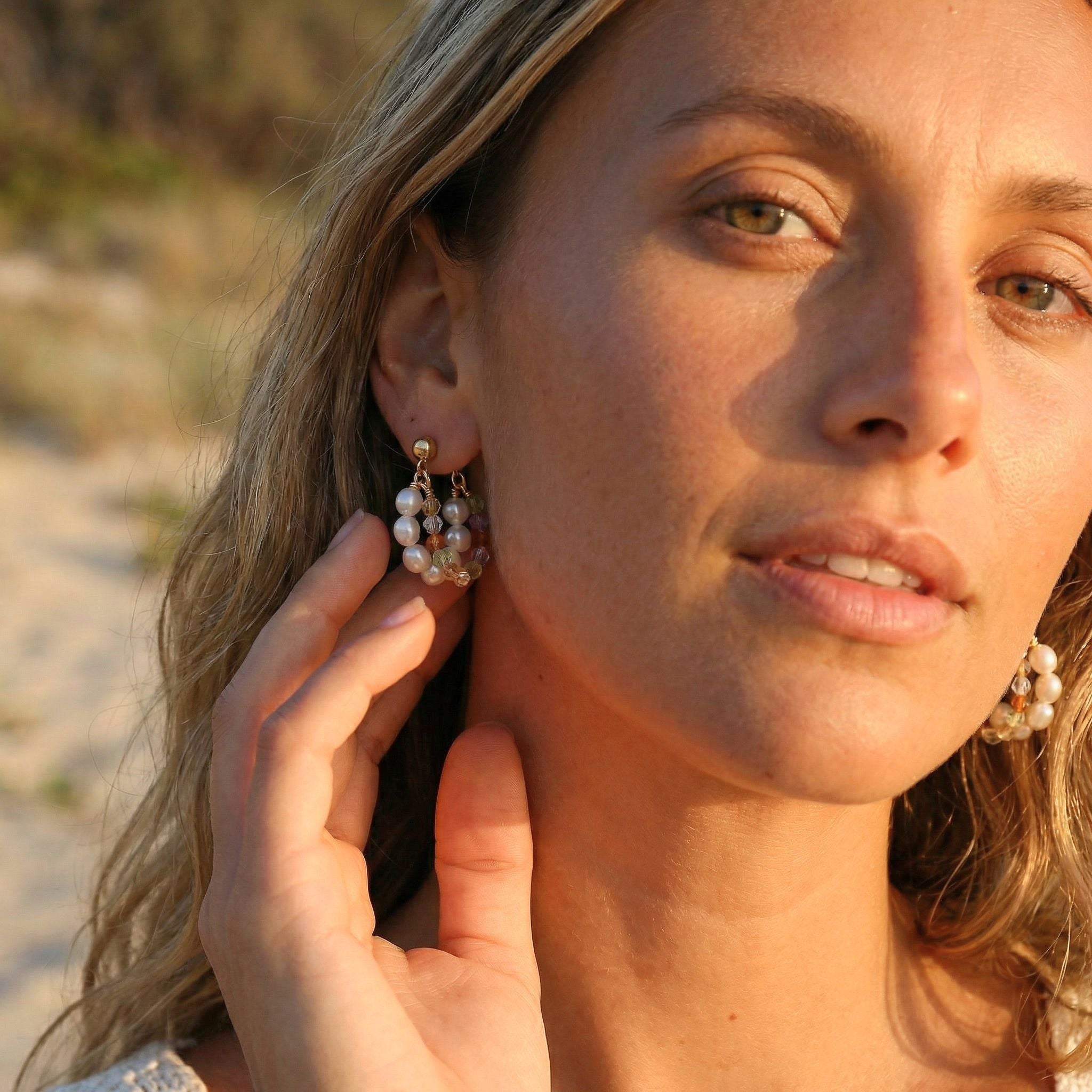 Woman adjusting pearl earrings on a beach