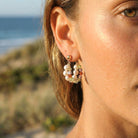 Close-up of a person wearing pearl earrings with a blurred beach background