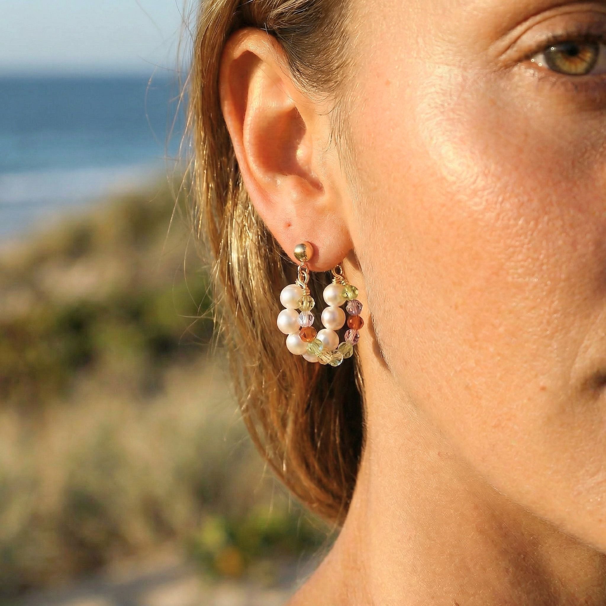 Close-up of a person wearing pearl earrings with a blurred beach background