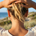 Person with blonde hair and earrings standing on a beach