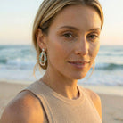 Woman on a beach wearing earrings with a blurred ocean background