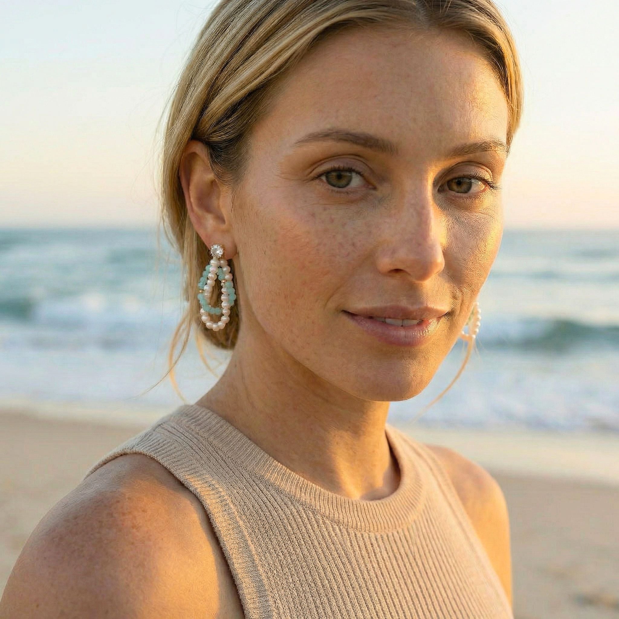 Woman on a beach wearing earrings with a blurred ocean background