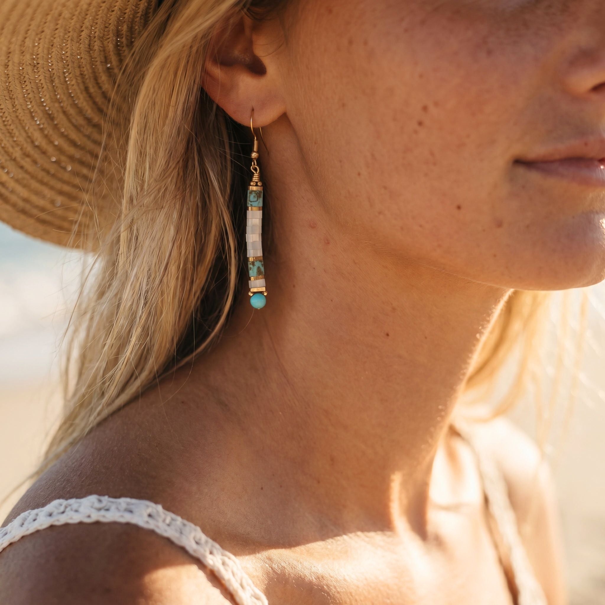 Close-up of a woman wearing a straw hat and gold earrings with turquoise stones.