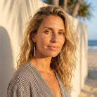 Woman with blonde hair and earrings standing on a beach with palm trees in the background