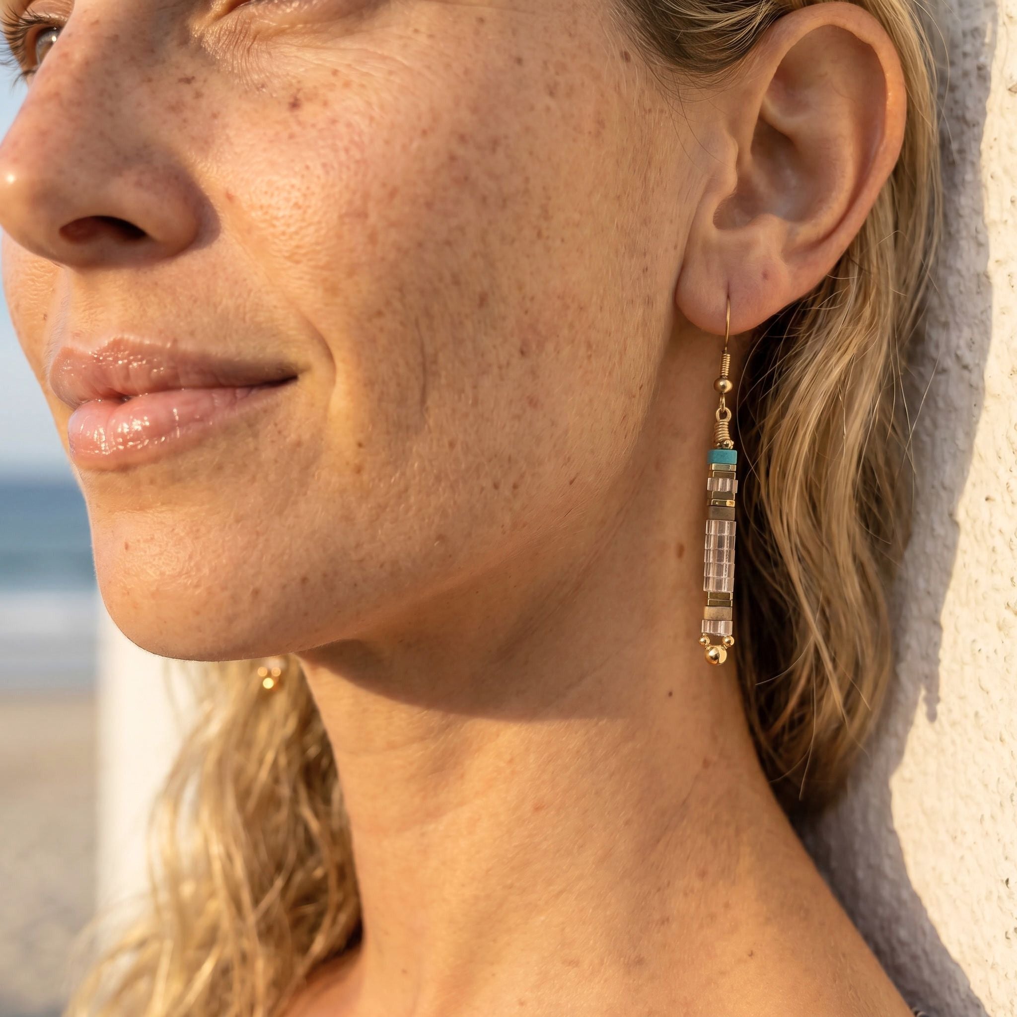 Close-up of a woman wearing gold earrings with a blurred beach background