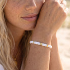 Close-up of a person wearing a white and gold bracelet with a blurred background