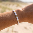 Close-up of a wrist wearing a white and gold bracelet against a blurred natural background