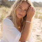 Woman in a white dress sitting in a natural setting with jewelry on.