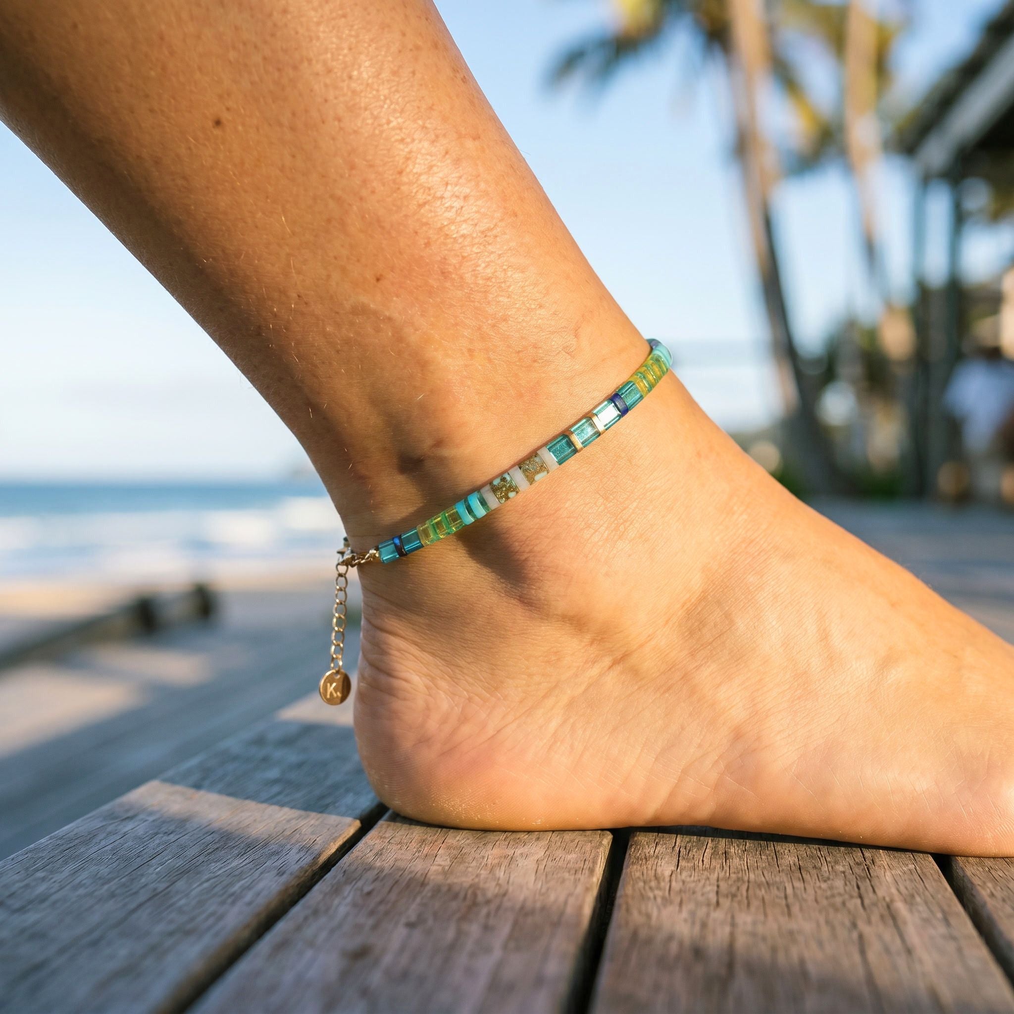 Anchored anklet on a foot with a beach and palm trees in the background