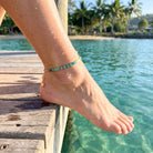 Person's foot with anklet on wooden dock by clear water