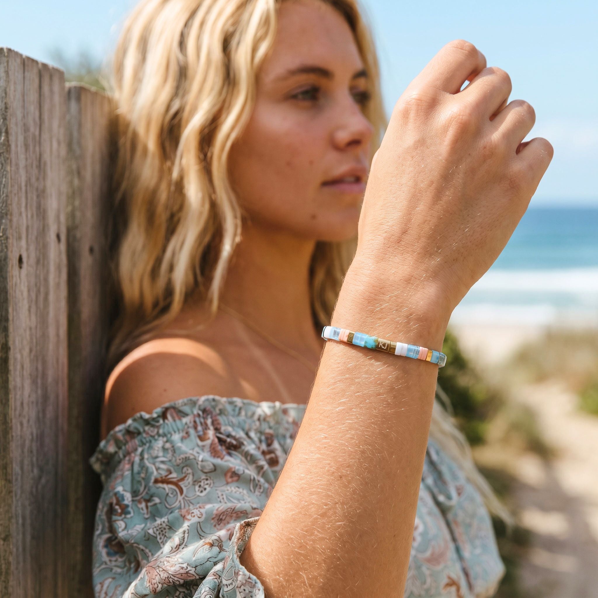 Woman wearing a colorful bracelet by a wooden fence with a beach in the background