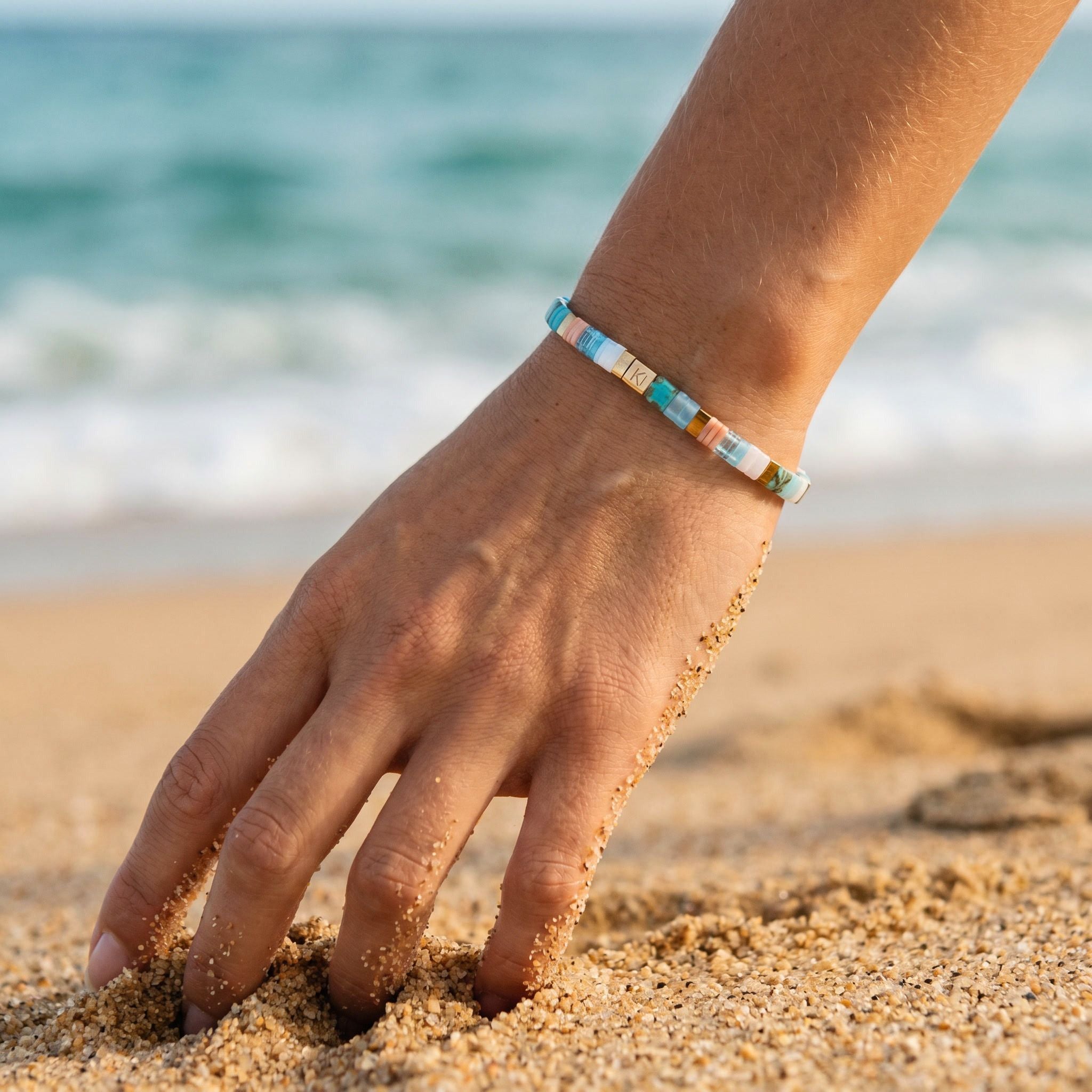 Hand with a colorful bracelet on a sandy beach with ocean in the background