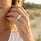 Close-up of a hand wearing a gold ring with a blurred natural background