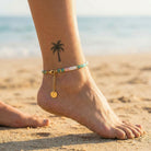 Anchored foot with gold anklet and green bracelet on sandy beach