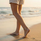 Person walking on a beach with feet and anklets visible
