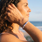 A woman in profile at the beach wearing a beaded bracelet made of pastel pink, lavender, and white beads.