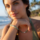 Woman on a beach with jewelry, wearing a green top and bracelets.