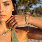 Woman wearing a green beaded necklace and bracelet outdoors with palm trees in the background