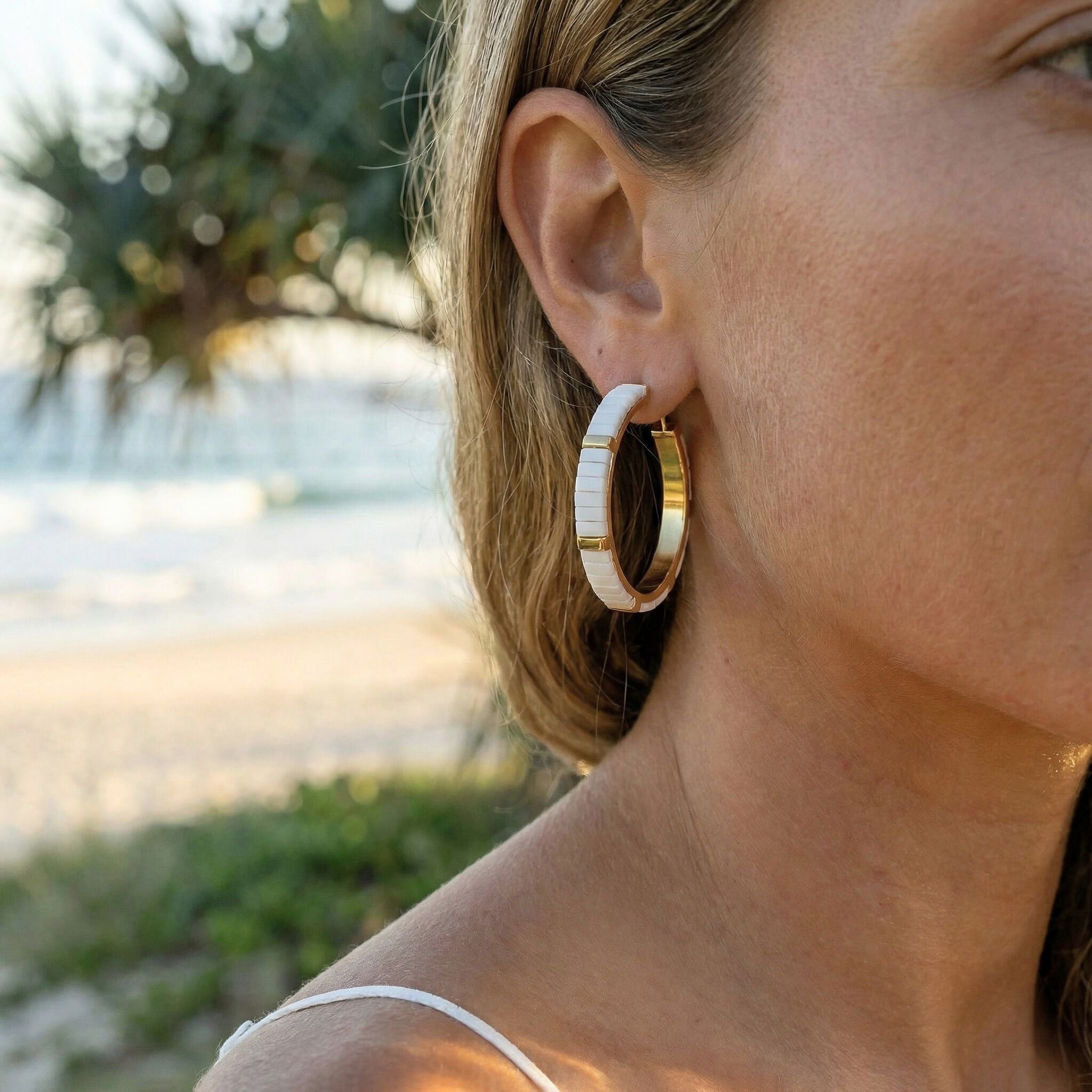 Close-up of a person wearing gold hoop earrings with a blurred natural background