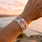 Close-up of a wrist wearing multiple bracelets with a blurred beach sunset background