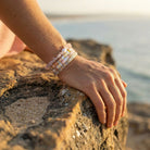 Hand wearing a bracelet on a rocky surface with a blurred natural background