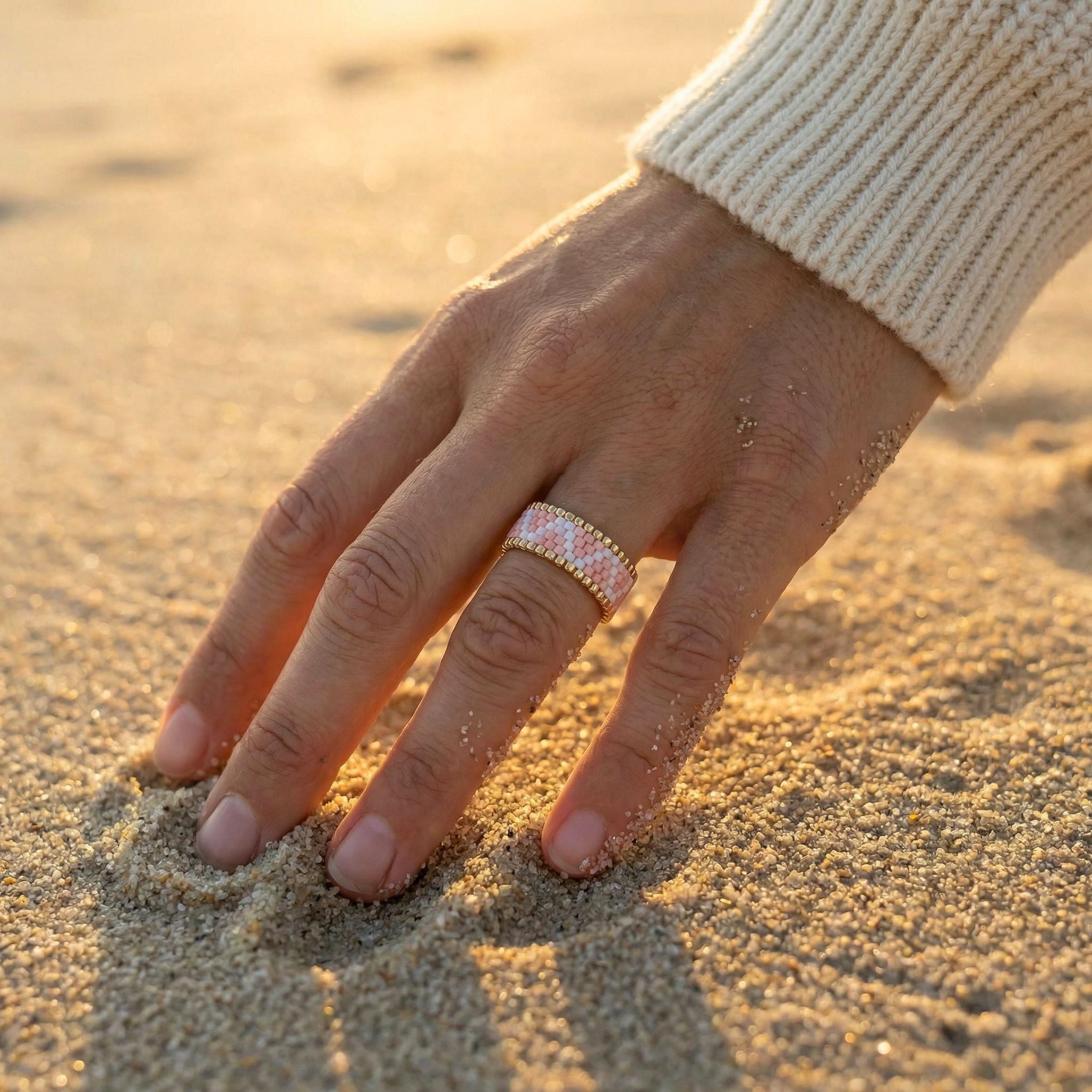Hand with a ring on a sandy surface
