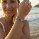 Woman on a beach wearing a colorful beaded bracelet and gold ring.
