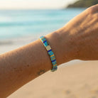 Bracelet with blue and gold accents on a wrist against a beach background