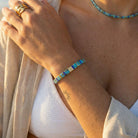 Close-up of a person's arm wearing a blue beaded bracelet with a sun tattoo, against a neutral background.