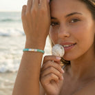 Woman holding a shell on a beach with a blurred background